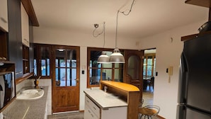 A kitchen with a central island, a sink, a refrigerator, and a dining area visible through a glass door. - Casa Las Colinas by Vilvey Turismo (Chacras de Coria)