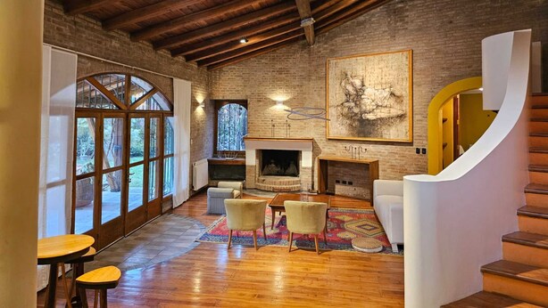A spacious living area with a fireplace, wooden flooring, and a large window overlooking a garden. - Casa Las Colinas by Vilvey Turismo (Chacras de Coria)
