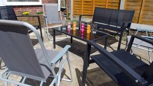 Eine Terrasse mit Glastisch, Metallstühlen und einer Bank.