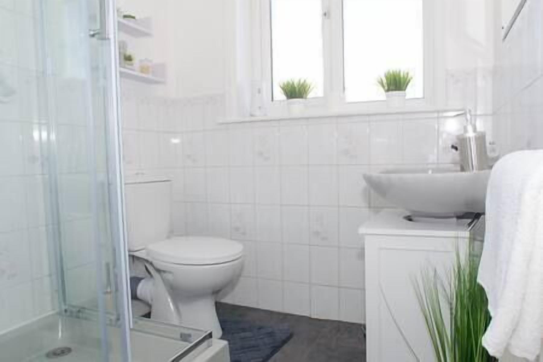 Un baño moderno con cabina de ducha de vidrio, inodoro blanco y lavamanos con espejo.