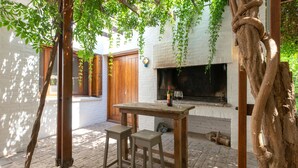 A rustic outdoor seating area with a wooden table and two stools, a brick floor, and a white brick wall. - Posada del huerto by Vilvey Turismo (Chacras de Coria)