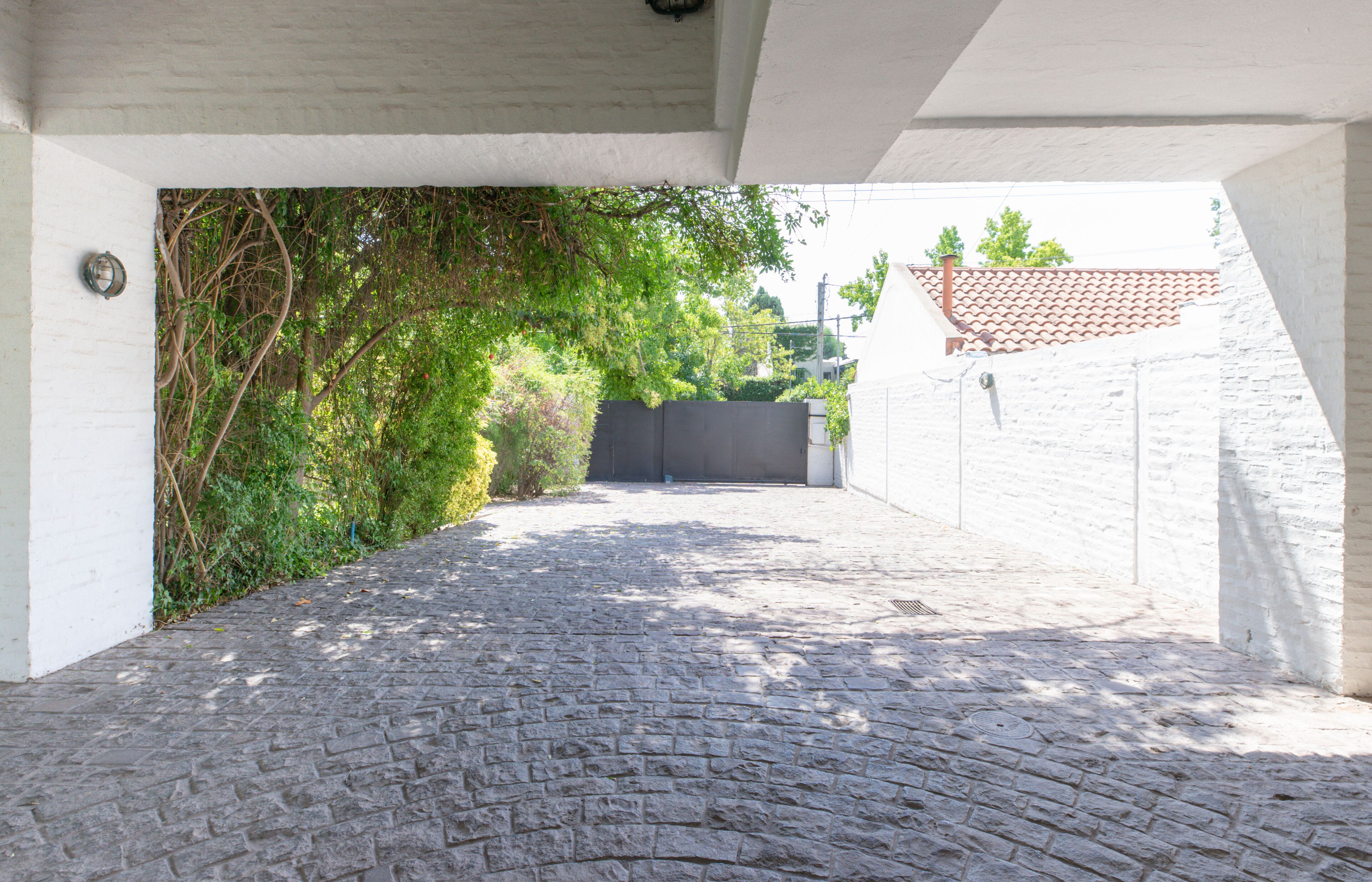 Un viale acciottolato che conduce a un cancello, circondato da muri bianchi e vegetazione.