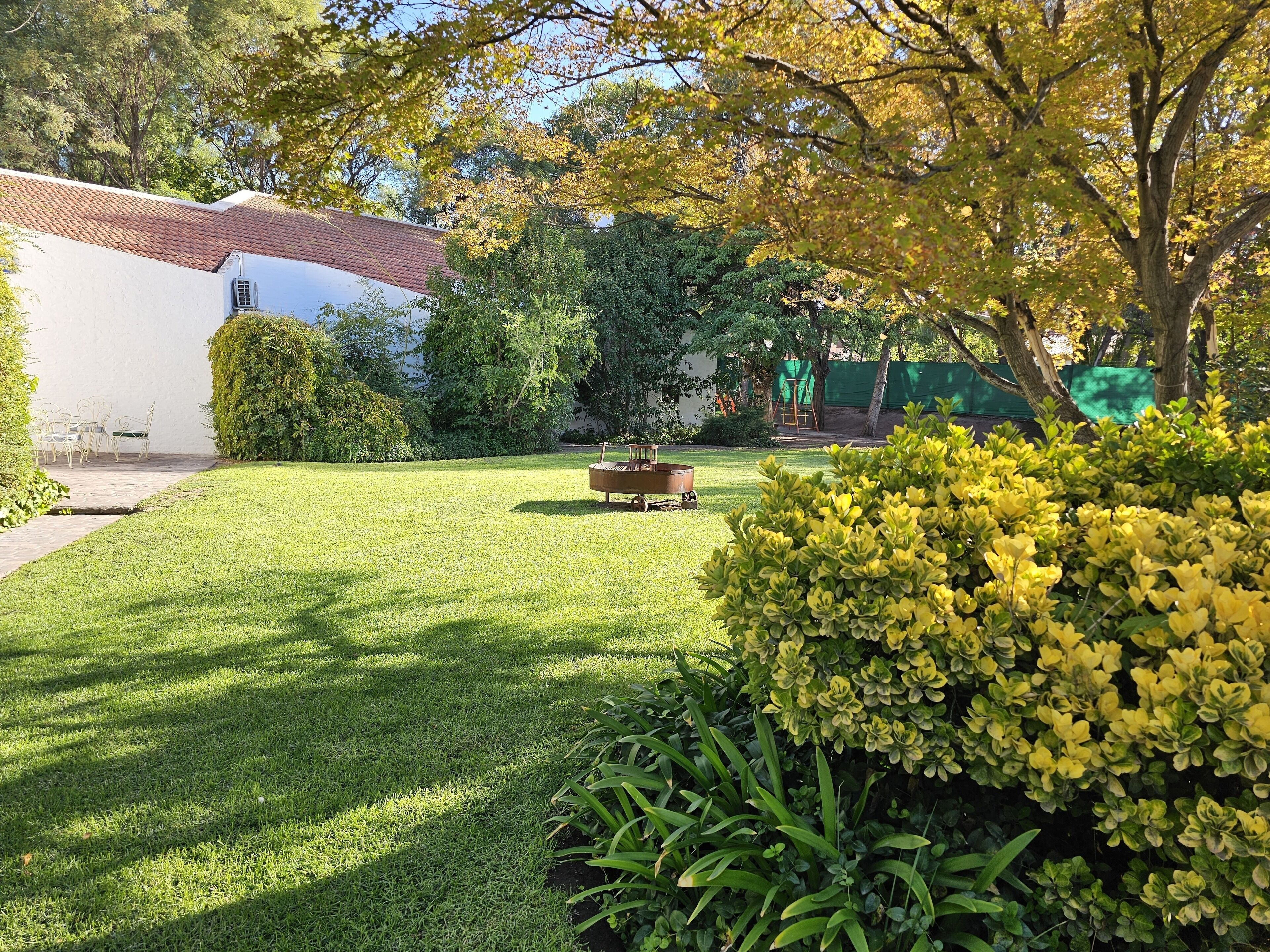A well-maintained garden with a lawn, a wooden bench, and a white building with a red roof.