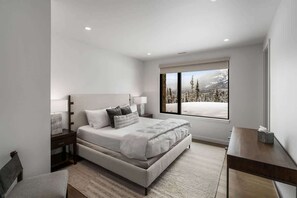 Um quarto moderno com uma cama grande, uma mesa de cabeceira e vista para uma paisagem nevada pela janela.