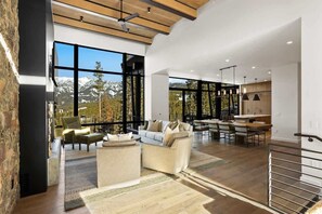 A spacious living area with a large window offering a mountain view, a cozy seating area with a sofa and chairs, and a modern kitchen in the background.