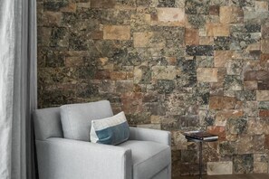 A room with a stone wall and a grey sofa with a pillow.
