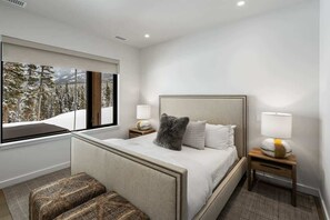 A modern bedroom with a large window, a bed with a headboard, two bedside tables with lamps, and a bench. - Luxury Ski-In/Ski-Out Moonlight Basin Home (Big Sky)