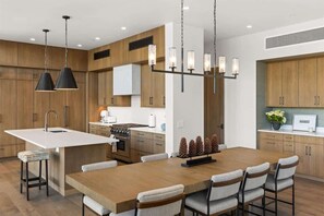 A modern kitchen with a central island, pendant lighting, and wooden cabinetry. - Luxury Ski-In/Ski-Out Moonlight Basin Home (Big Sky)