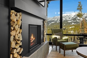 A fireplace with a stone surround, a view of snow-capped mountains, and two green chairs by the window. - Luxury Ski-In/Ski-Out Moonlight Basin Home (Big Sky)