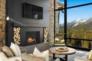 A modern living room with a fireplace, comfortable seating, and a large window offering a mountain view.
