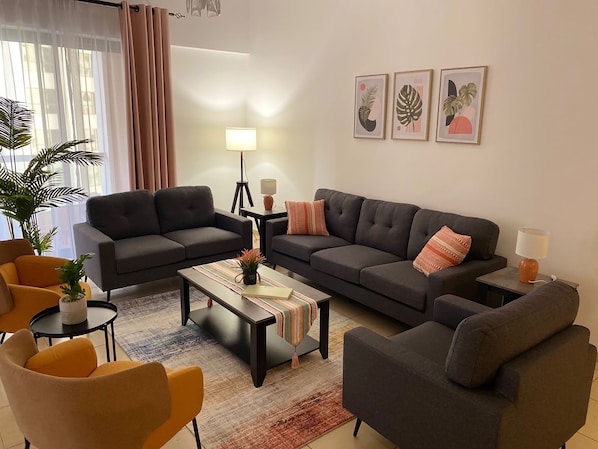 Un salon moderne avec deux canapés gris, une table basse et une petite table d’appoint avec une lampe. Trois reproductions botaniques encadrées ornent le mur.