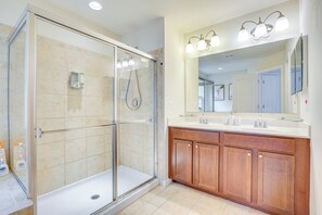 Un baño moderno con ducha envuelta en vidrio, tocador de madera y un espejo grande.