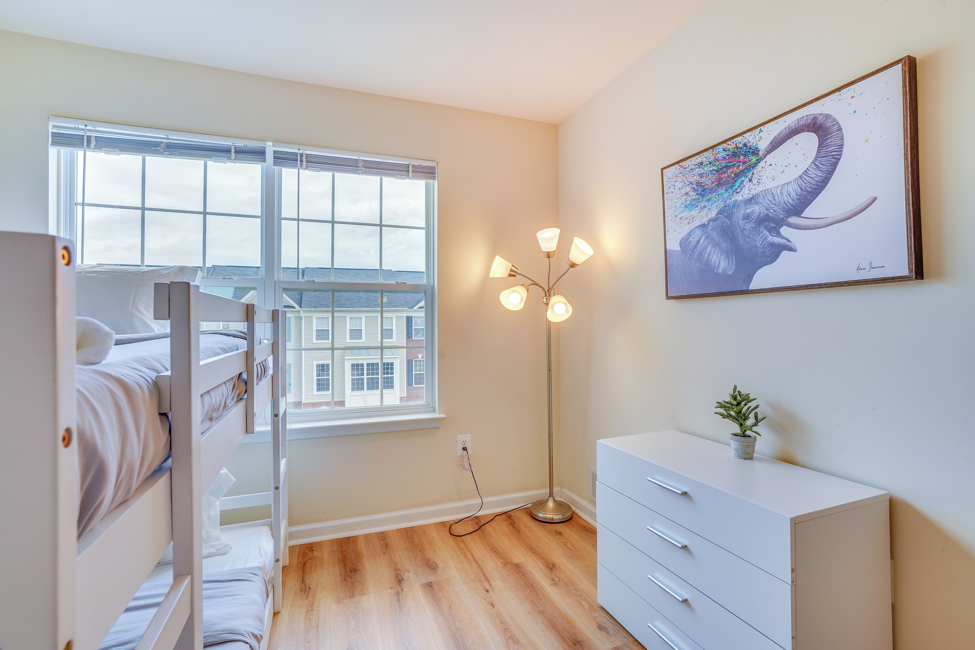 A room with bunk beds, a floor lamp, a dresser, and a painting of an elephant.