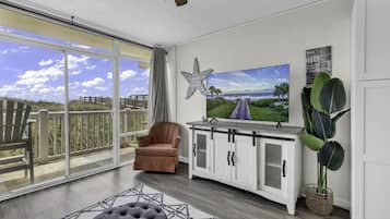Een ruim balkon met uitzicht op het strand, een comfortabele bruine stoel, een grote flatscreen-tv en een decoratieve zeester aan de muur.