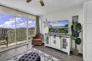Ein geräumiger Balkon mit Blick auf den Strand, ein bequemer brauner Sessel, ein großer Flachbildfernseher und ein dekorativer Seestern an der Wand.