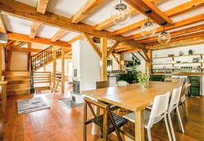 A spacious kitchen with wooden beams, a dining area with a large table, and a staircase leading to another level.