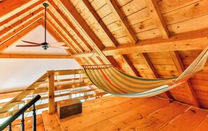 A hammock suspended from a wooden ceiling in a cabin with a staircase and a ceiling fan.