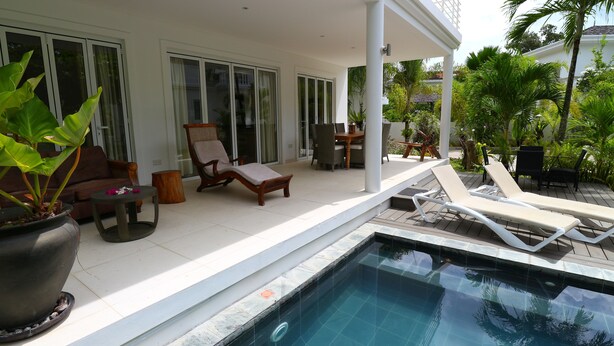 A poolside area with a lounge chair, a wooden table, and a potted plant. - Las Brísas Villa - Chateau Elysium (Mahé Island)