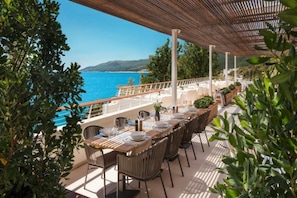 An outdoor dining area with tables set for a meal, overlooking a body of water. - Girandella Resort Valamar Collection - Family Hotel (Labin)