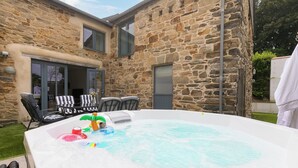 Ein Steinhaus mit Whirlpool, Sitzgelegenheit im Freien und einer Glasdoor, die zu einer Terrasse führt.