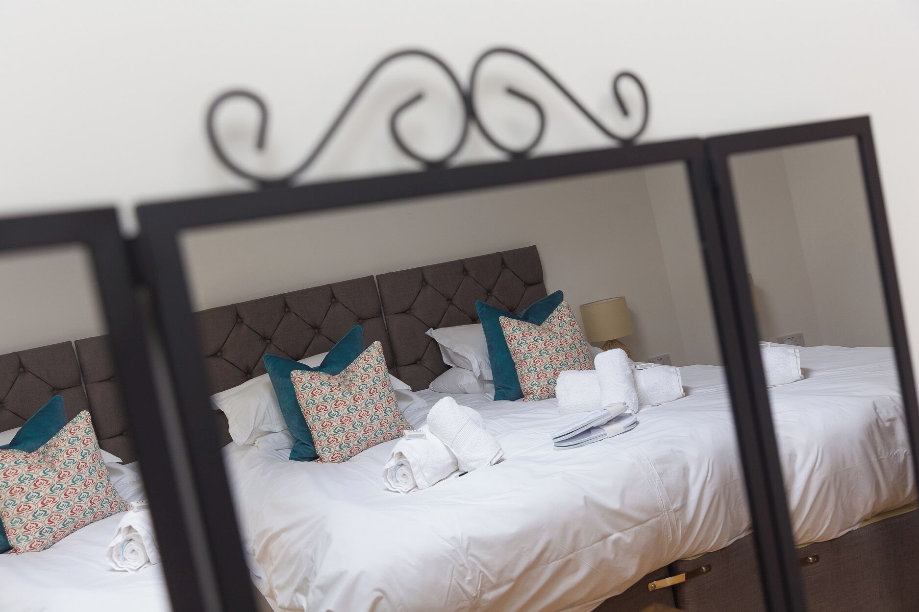 A neatly made bed with white linens, a tufted headboard, and patterned pillows.