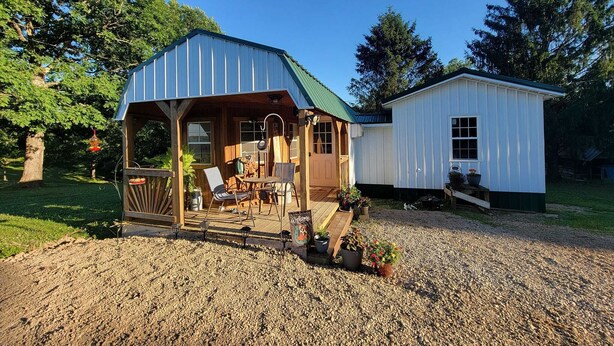 A rustic cabin with a covered porch, a small attached shed, and a gravel driveway. - Newly transformed farm cottage off the beaten path! (Minford)