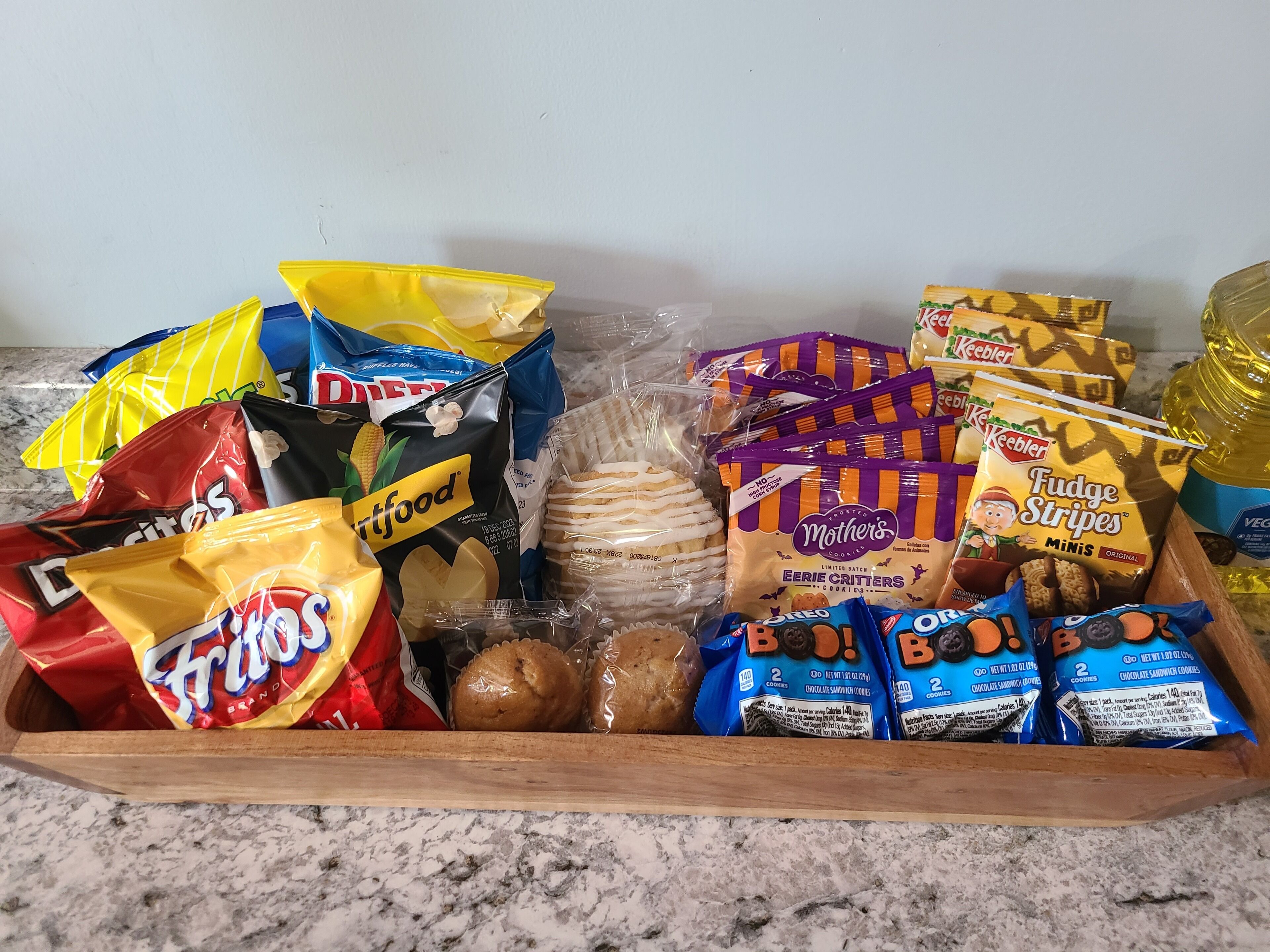 Een schaal met diverse lekkernijen, zoals chips, koekjes en crackers.
