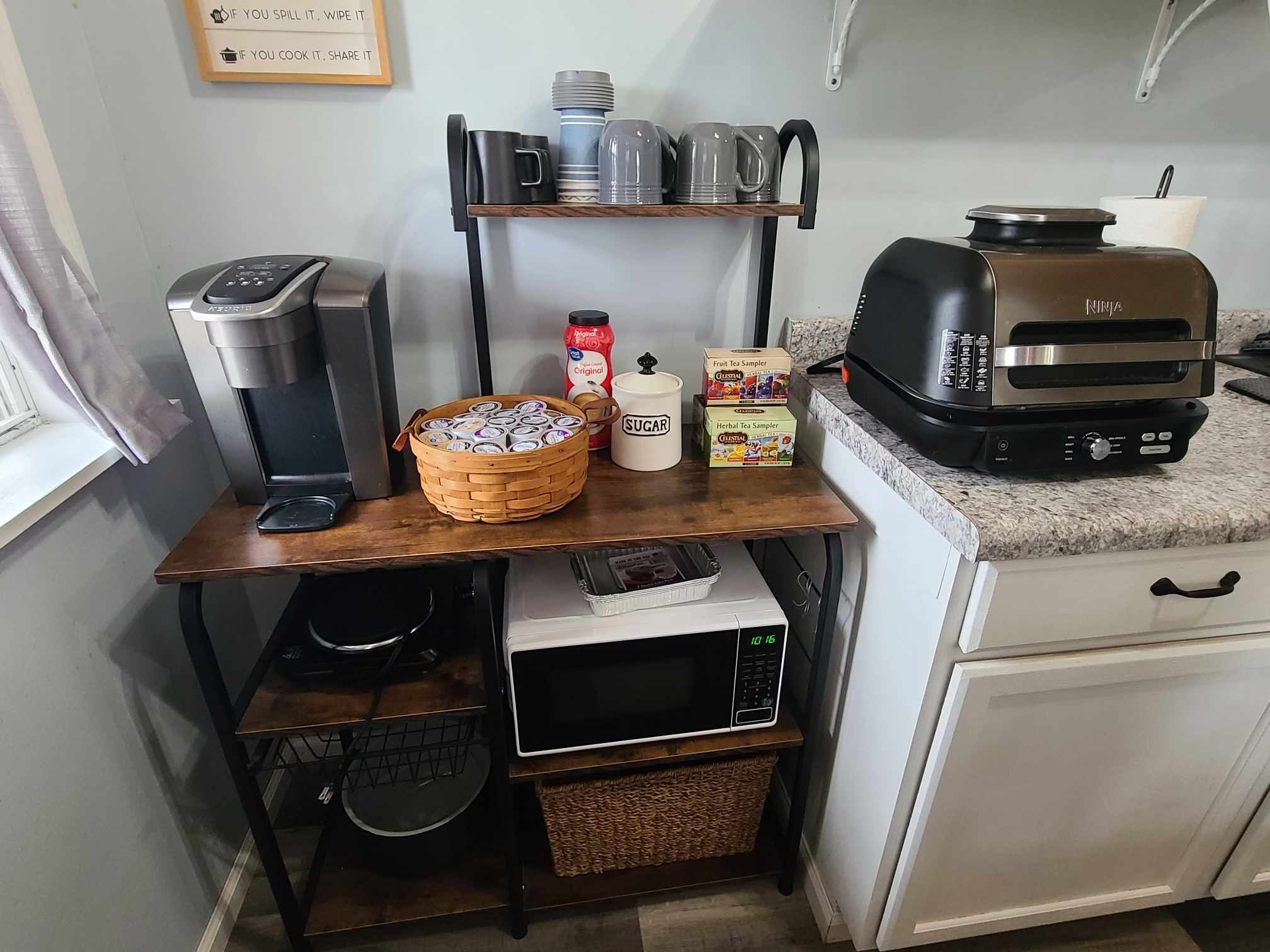 A kitchen with a coffee maker, tea samplers, a sugar container, and a microwave.