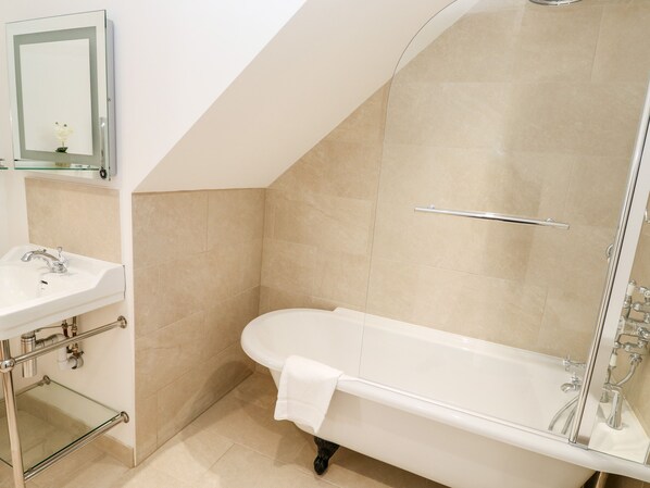 A bathroom with a freestanding bathtub, a glass shelf above the sink, and a mirror with a small flower decoration.