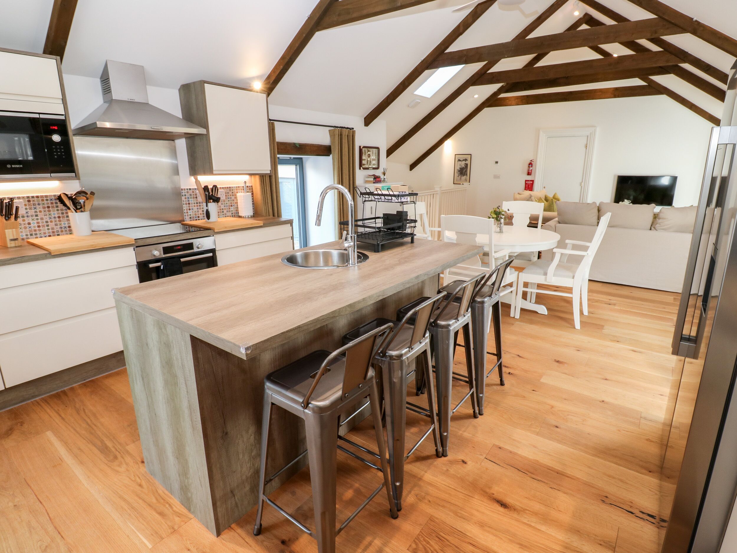 A modern kitchen with a central island, bar stools, and a dining area with a white table and chairs.