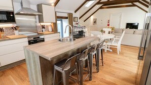 Una cocina moderna con una isla central, taburetes de bar y una zona de comedor con una mesa y sillas blancas.