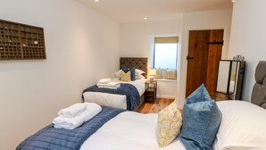 Habitación de hotel con dos camas, ventana con vistas, puerta de madera y una mesita con lámpara.