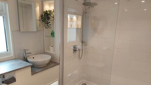 Une salle de bain moderne avec un lavabo blanc, une douche en verre et une petite fenêtre.