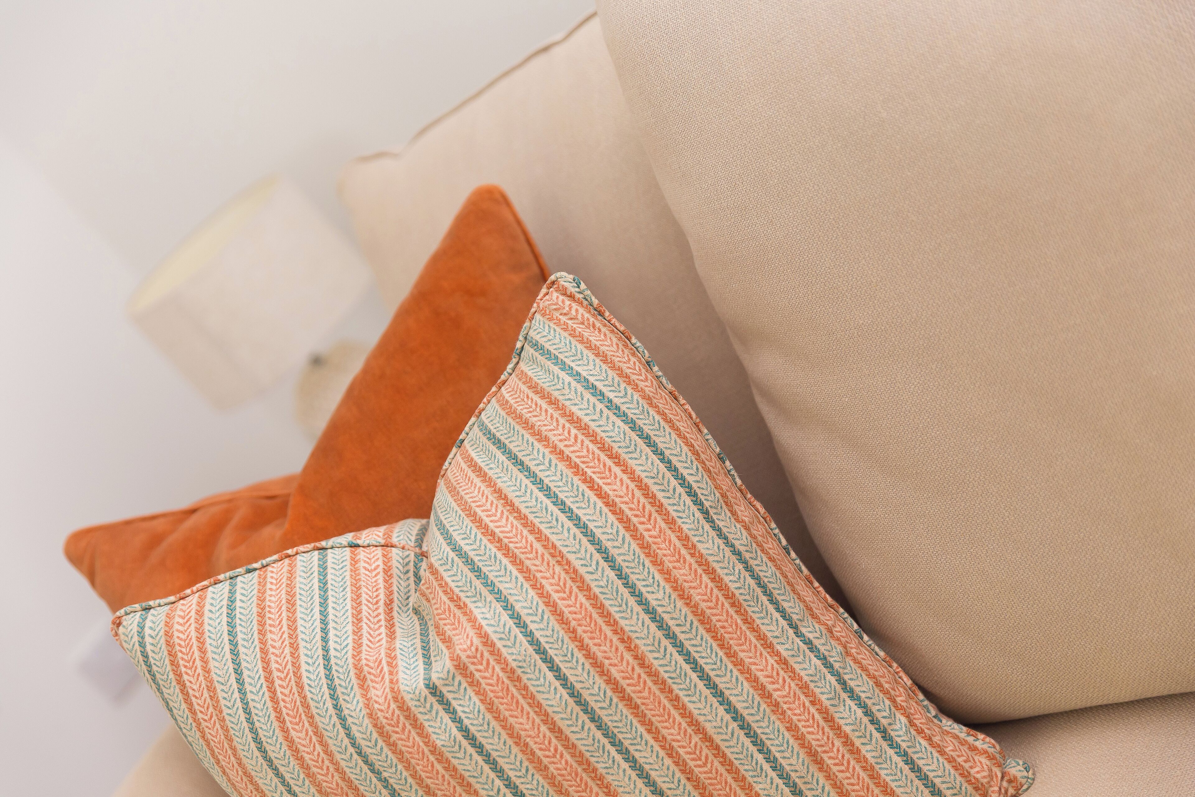 A beige sofa with two pillows, one striped and one solid orange.