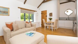 A spacious living room with a sofa, a dining area with a table and chairs, and a kitchen with a sink and cabinets. - Carines Barns - Tre (Newquay)