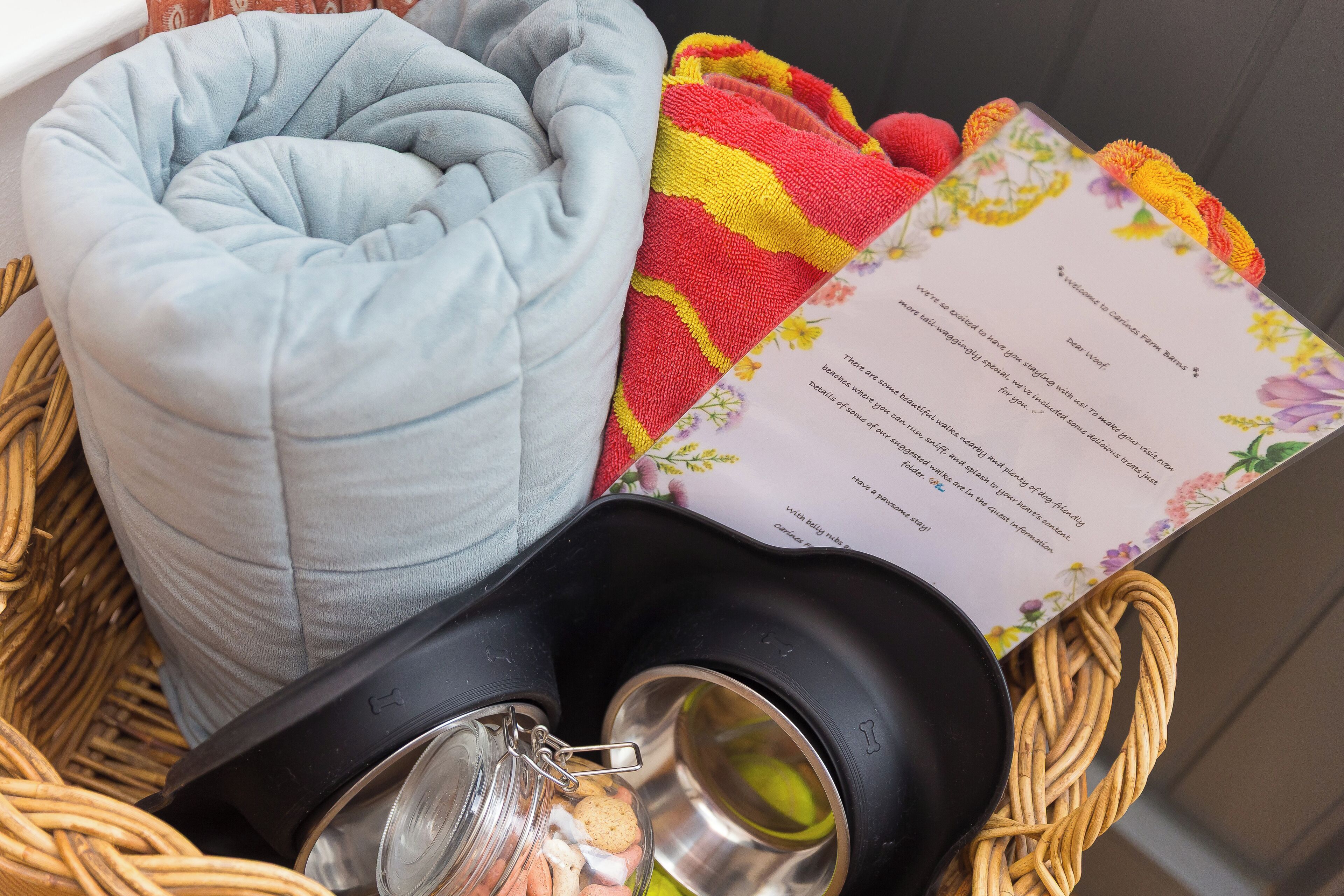 A basket containing a light blue cushion, a black water bottle, a woven basket, and a menu with floral designs.