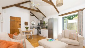 A modern living room with a sofa, ottoman, and a dining area with a table and chairs. - Carines Barns - Tre (Newquay)