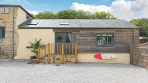 A small stone building with a wooden extension, a wooden staircase, and a surfboard leaning against the wall. - Carines Barns - Tre (Newquay)