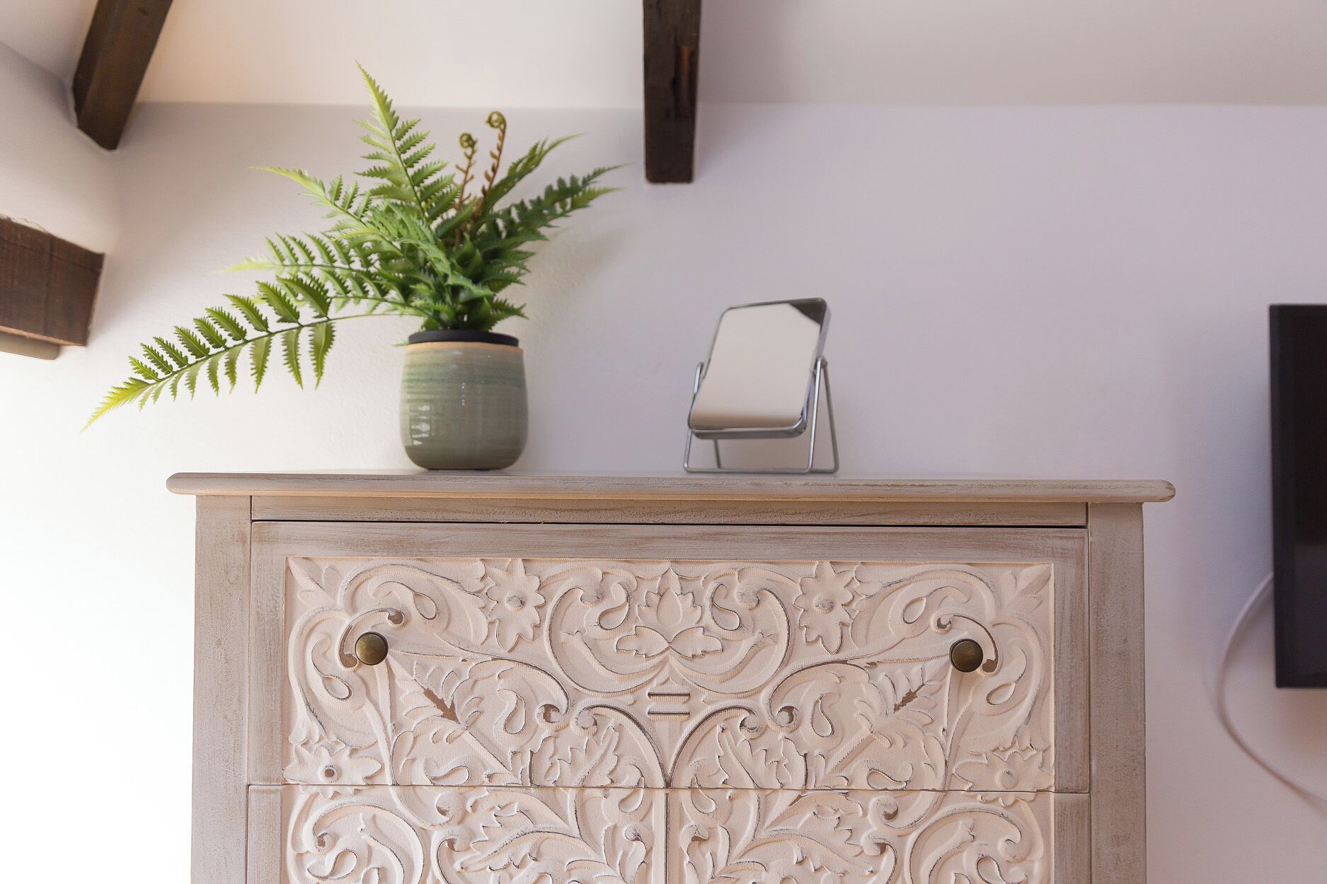 A light-colored, intricately carved wooden cabinet with a plant and a small metal stand on top.