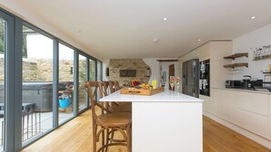 A modern kitchen with a central island, large windows, and a stone wall. - Carines Barns - Wesley Barn (Newquay)