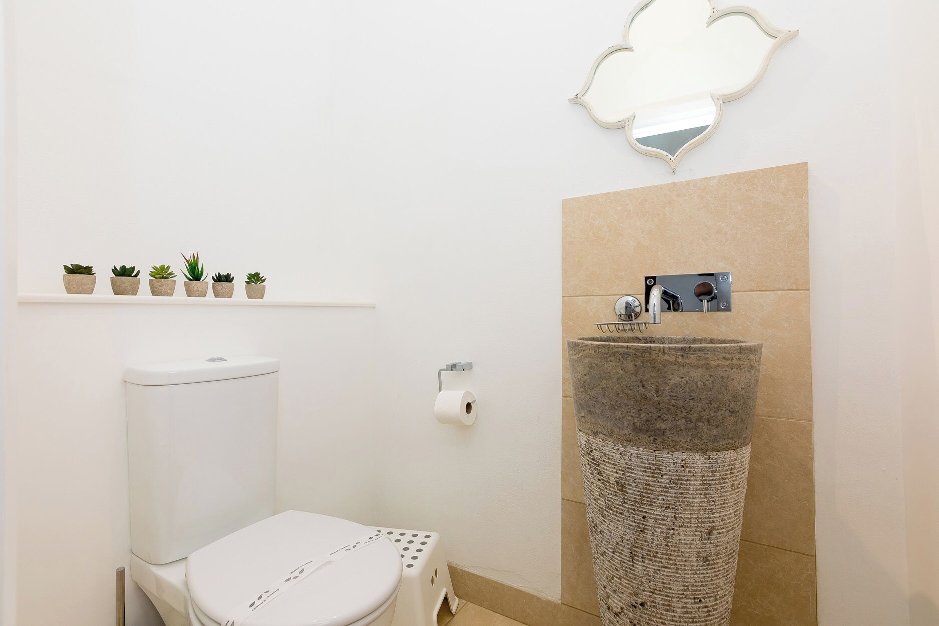 A bathroom with a toilet, sink, and a shelf with potted plants.