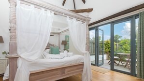 A four-poster canopy bed with a wooden frame and white bedding, a glass door leading to a balcony with outdoor furniture, and a view of greenery. - Carines Barns - Wesley Barn (Newquay)