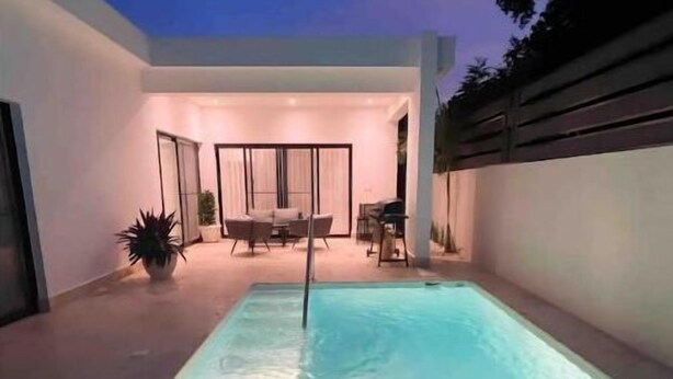 Zona de piscina exterior moderna, piscina cristal·lina, zona d'estar amb taula i cadires, i un porxo cobert.