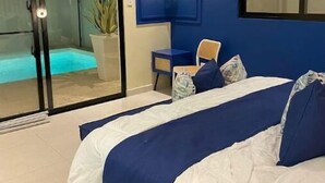 Un dormitori amb un llit, una cadira, una planta en test i una porta corredissa de vidre que dona a un balcó.