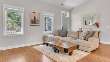 Una sala de estar con sofá color beige, una mesa de centro y un ventanal con persianas.
