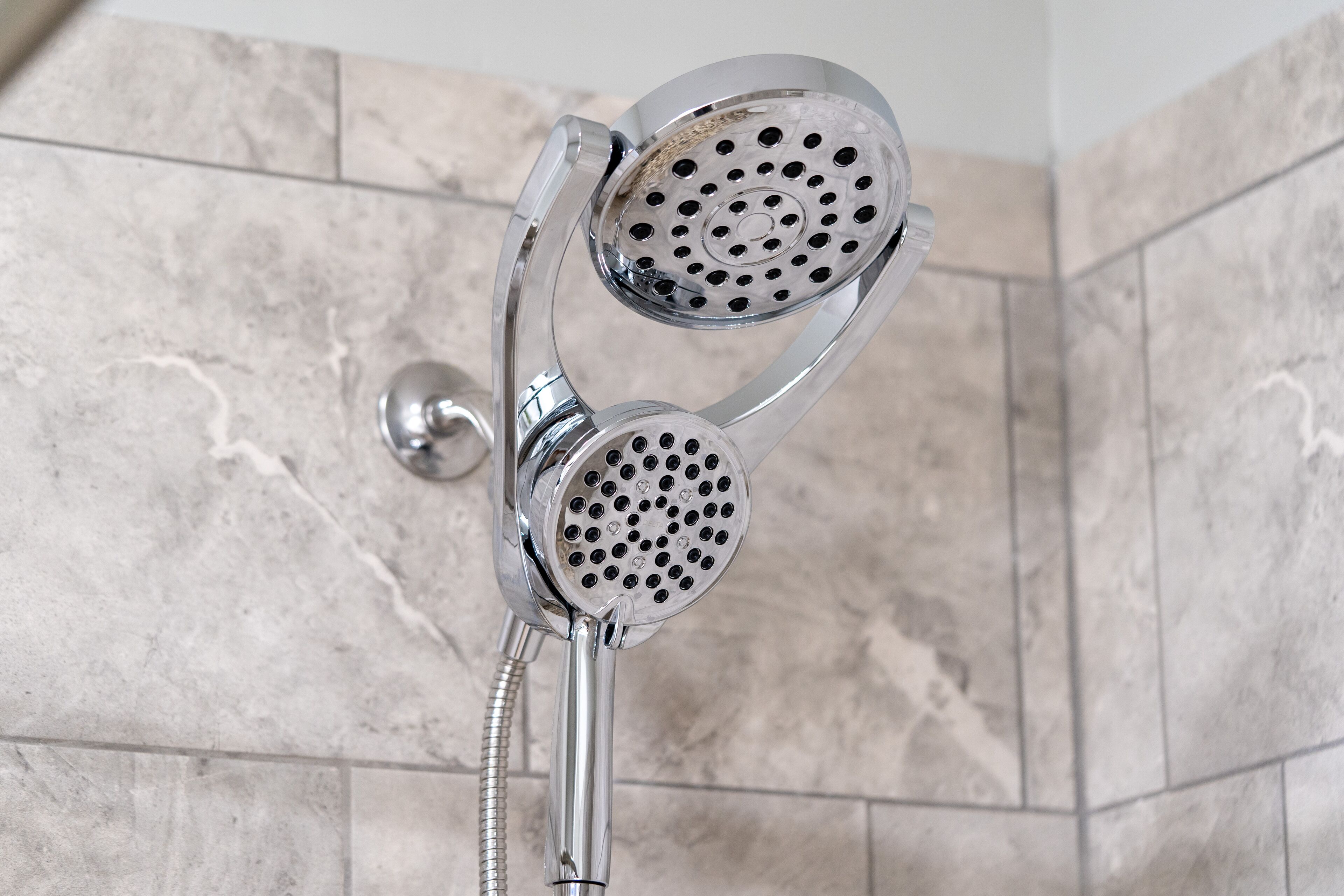A showerhead with a flexible hose, mounted on a wall with a tiled surface.