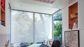A modern bedroom with a large window, a bed, a small table, and a staircase. - Kasita Nest is a prefabricated, smart home for romantic getaways. (Austin)