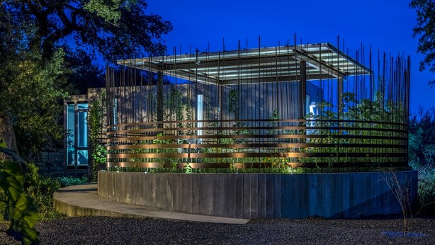 A modern glass structure with vertical supports, surrounded by greenery and a concrete base. - Kasita Nest is a prefabricated, smart home for romantic getaways. (Austin)