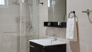 Un baño moderno con ducha de vidrio, tocador negro con espejo y lavamanos blanco.