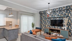 Una sala moderna con un sofá gris, una mesita de centro pequeña y un televisor sobre un mueble de madera.